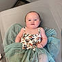Paisley is registered to the contest to win money with this photo: baby, infant, child, tutu, floral_clothing, fabric, soft_texture, gray_surface, lying_down, curious_expression, cute, indoors, skin, foot, hand, face, head, plump, sitting, person