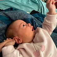 Aria is registered to the contest to win money with this photo: baby, infant, child, bed, blanket, blue_blanket, teal_blanket, pink_clothing, heart_design, hand, face, ear, skin, lying_down, indoor, soft_fabric, cute, young_child, expression, reaching_hand