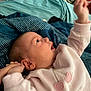 baby, infant, child, bed, blanket, blue_blanket, teal_blanket, pink_clothing, heart_design, hand, face, ear, skin, lying_down, indoor, soft_fabric, cute, young_child, expression, reaching_hand