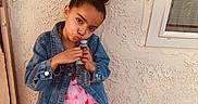 Arianna is registered to the contest to win money with this photo: child, girl, denim_jacket, pink_dress, hearts, water_bottle, pouting, hairstyle, top_bun, standing, wall, window, outdoor, cute, playful, fashion, portrait, person, smile, clothing