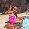Arianna joined the competition — help win amazing prizes! child, girl, swimsuit, pool, water, peace_sign, smile, outdoor, sunny, backyard, brick, fence, concrete, sitting, playful, summer, recreation, young, person, happy