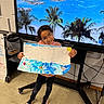 child, drawing, artwork, classroom, floor, screen, beach, palm_trees, blue_sky, glasses, shoes, jeans, smile, presentation, paper, indoor, technology, cables, educational, happy