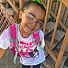Arianna is registered to the contest to win money with this photo: child, girl, glasses, green_bow, backpack, tshirt, sidewalk, stairs, concrete, outdoor, smiling, portrait, casual_clothing, young, happy, fashion_accessory, person, urban, daylight, playful