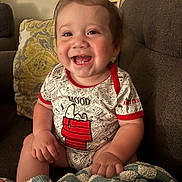 Andrew joined the competition — help win amazing prizes! baby, smiling, child, onesie, snoopy, couch, pillow, blanket, indoor, happy, cute, portrait, infant, toddler, clothing, face, hand, hair, seated, cozy