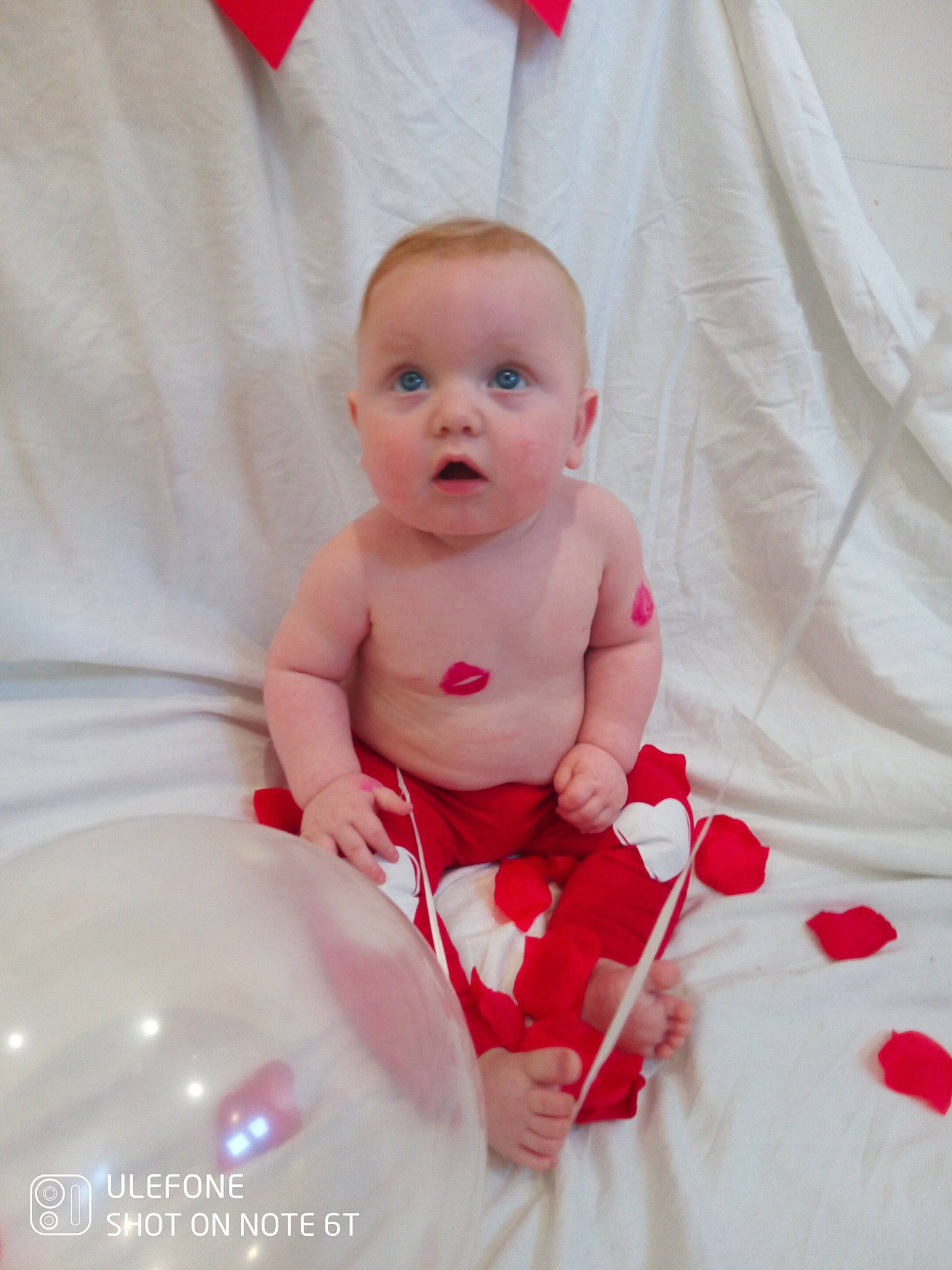 Ares is registered to the contest to win money with this photo: arm, baby, baby_products, baby_toddler_clothing, carmine, cheek, comfort, event, eye, fun, happy, human_body, linens, nail, person, petal, sitting, sleeve, stomach, surprise