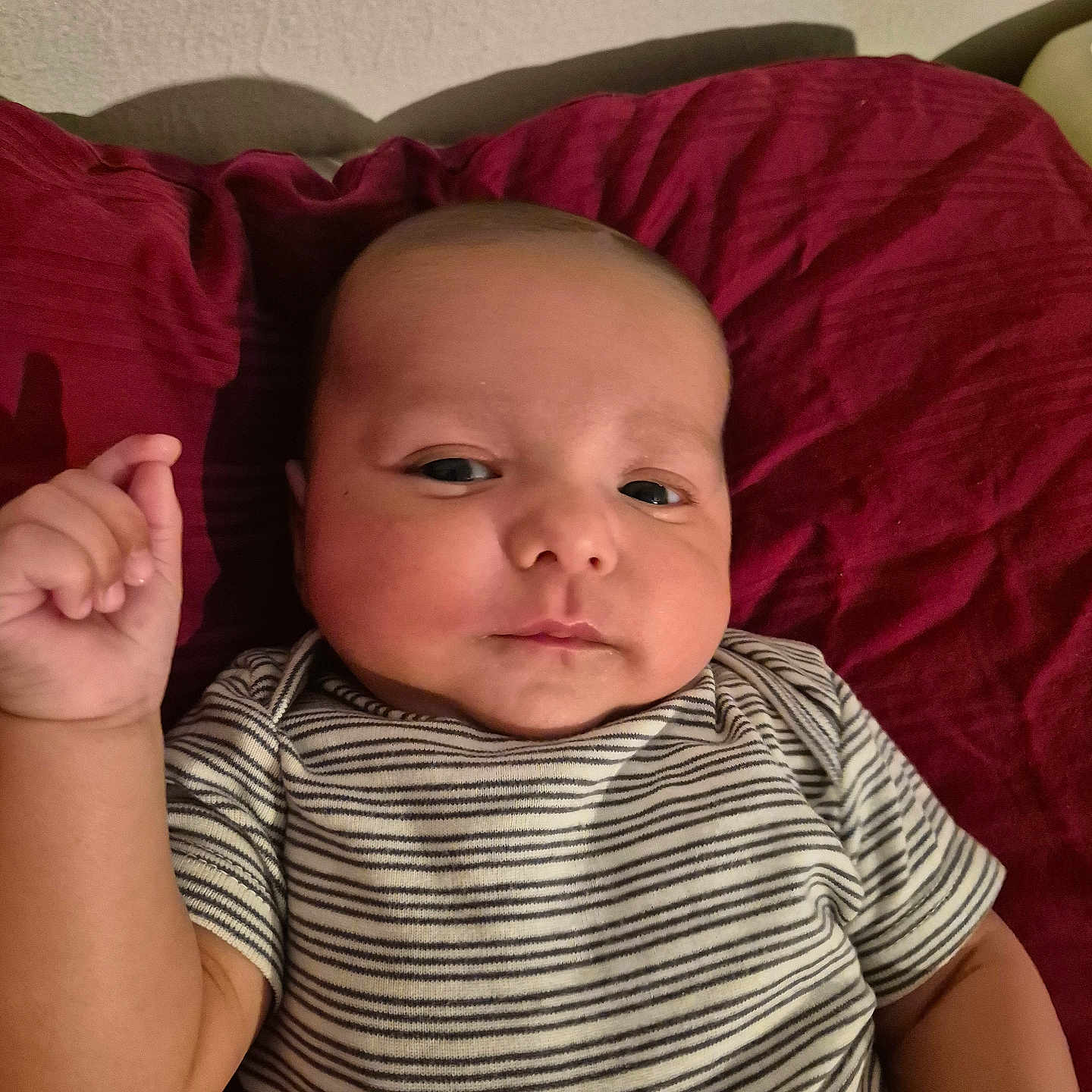 Jonas joined the competition — help win amazing prizes! baby, infant, child, portrait, face, eyes, smiling, hand, raised_hand, striped_shirt, clothing, pillow, bed, indoors, home, red, warm_lighting, sitting, closeup, photography