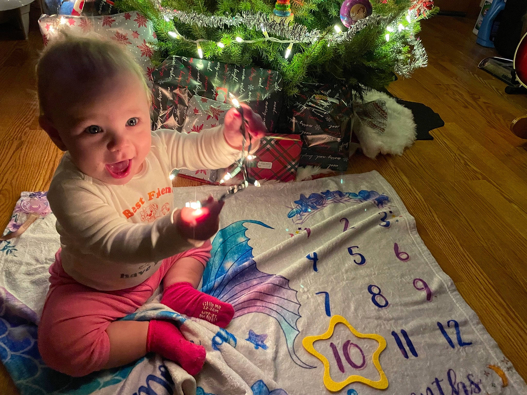Melody is registered to the contest to win money with this photo: baby_toddler_clothing, child, christmas_decoration, christmas_eve, christmas_ornament, christmas_tree, event, flooring, fun, happy, holiday, lap, ornament, person, plant, play, sitting, smile, toddler, tree