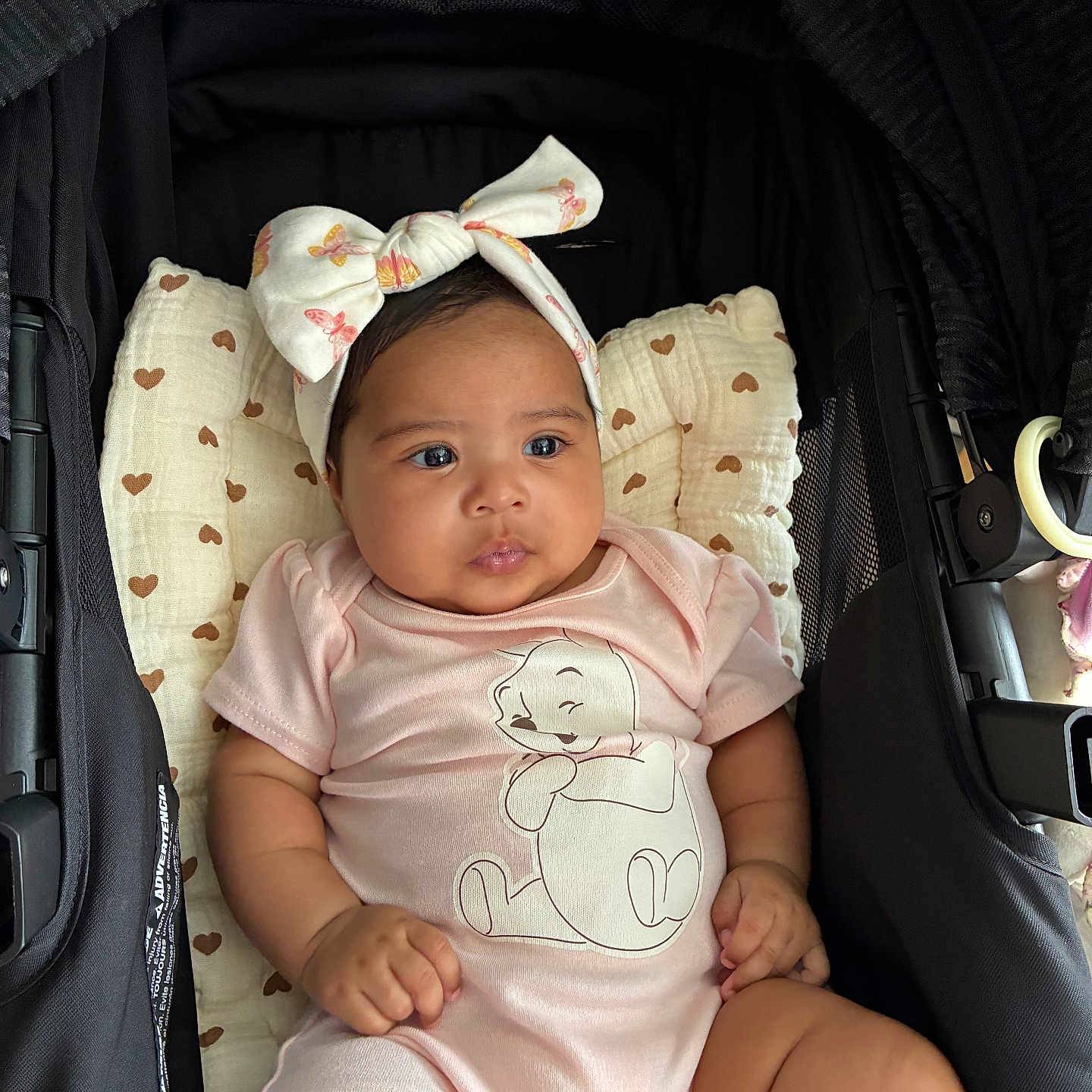 Mavie Ocean joined the competition — help win amazing prizes! baby, infant, child, stroller, onesie, headband, bow, cartoon, pink_clothing, pillow, heart_pattern, cute, indoors, relaxed, chubby, skin, hand, face, legs, seated