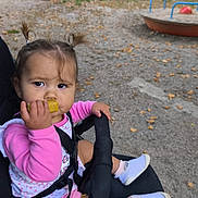Kaëly a rejoint le concours — aidez-le/la à gagner de superbes lots ! toddler, child, stroller, snack, pigtails, pink_clothing, outdoor, playground, fence, autumn_leaves, curious, socks, shoes, seatbelt, person, young_child, daylight, park, grip, baby