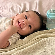 Liam Vasquez is registered to the contest to win money with this photo: baby, smiling, infant, blanket, bottle, lying_down, cute, happy, face, clothing, skin, head, person, baby_bottle, bed, resting, indoors, young_child, closeup, comfort