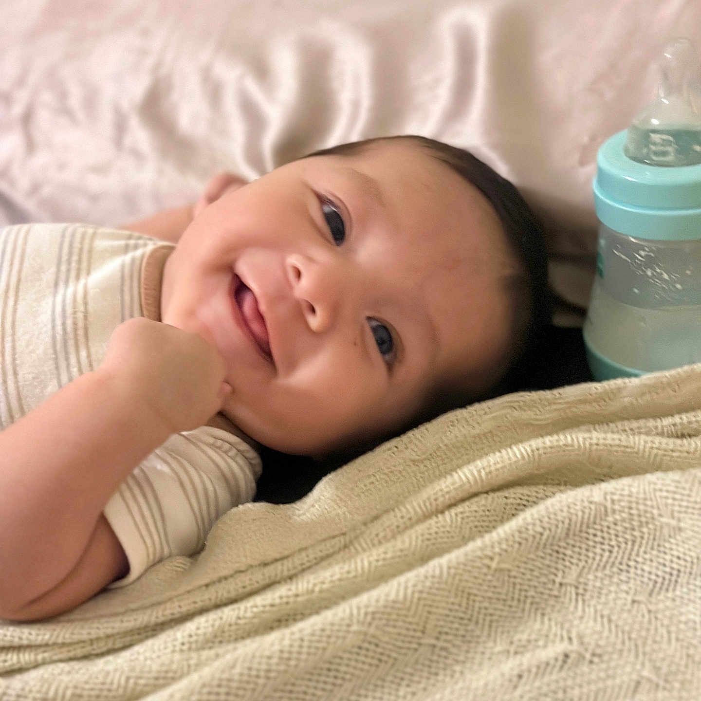 Liam Vasquez is registered to the contest to win money with this photo: baby, smiling, infant, blanket, bottle, lying_down, cute, happy, face, clothing, skin, head, person, baby_bottle, bed, resting, indoors, young_child, closeup, comfort