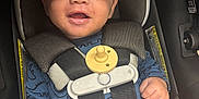 Ke-Shawn is registered to the contest to win money with this photo: baby, child, car_seat, safety_harness, pacifier, blue_clothing, dinosaur_print, smiling, happy, infant, cute, hands, legs, seatbelt, closeup, indoors, person, face, portrait, young_child