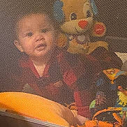 Ke-Shawn is registered to the contest to win money with this photo: baby, child, mesh_screen, toy, plush_dog, colorful, playpen, indoor, soft_focus, cute, smiling, infant, person, fabric, pattern, playtime, red_clothing, orange, blue, yellow