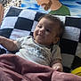baby, blanket, checkered_pattern, painting, portrait, indoor, child, face, head, smile, furniture, art, cozy, curly_hair, person, soft_texture, couch, toddler, clothing, relaxing