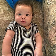 Ke-Shawn is registered to the contest to win money with this photo: baby, infant, striped_clothing, couch, blanket, indoor, child, face, portrait, curious, soft_furniture, cute, young_child, one_piece, patterned_fabric, relaxed, home, chubby_arms, seated, looking_up