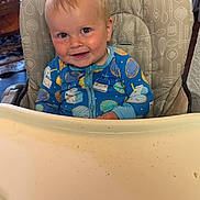Eli is registered to the contest to win money with this photo: baby, child, high_chair, onesie, blue_clothing, smiling, face, indoor, messy_tray, milk_carton_pattern, donut_pattern, cute, infant, happy, person, furniture, wooden_chair, table, home, portrait
