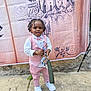 toddler, child, boy, pink_suit, bow_tie, braids, keys, white_shoes, concrete_floor, castle_backdrop, outdoor, standing, portrait, fashion, accessories, happy, cute, small_person, event, background