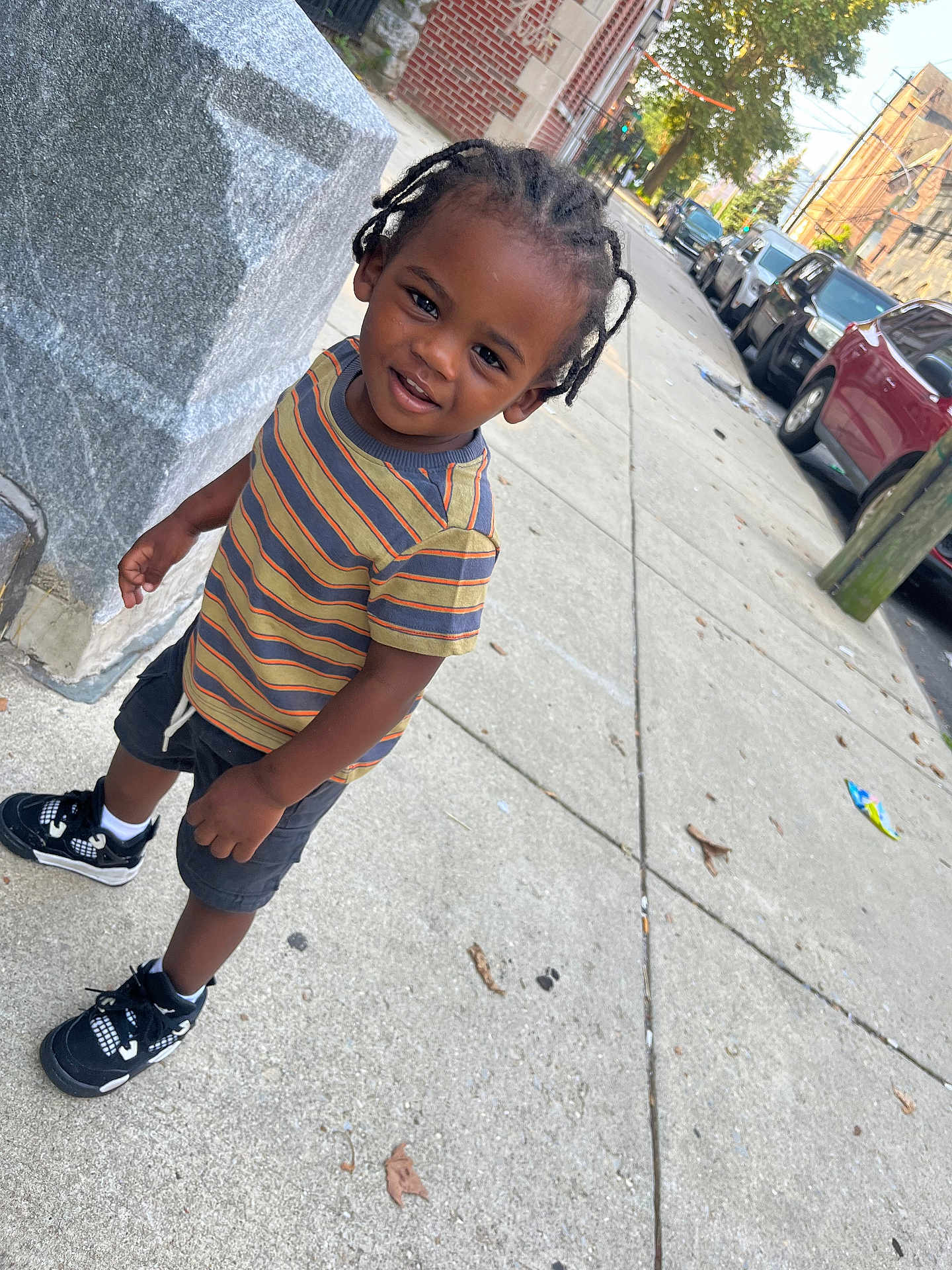 Noah joined the competition — help win amazing prizes! child, toddler, braids, striped_shirt, shorts, sneakers, sidewalk, urban, street, cars, curious, smile, outdoor, daylight, concrete, building, tree, person, young, casual_clothing
