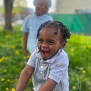 Noah is registered to the contest to win money with this photo: child, toddler, smiling, laughing, outdoor, grass, flowers, greenery, blurred_background, braided_hair, polo_shirt, bracelet, happy, two_children, nature, daylight, casual_clothing, portrait, playful, joy