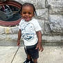 Noah is registered to the contest to win money with this photo: child, toddler, smiling, standing, sidewalk, stone_wall, braids, white_tshirt, dinosaur_graphic, black_shorts, black_sneakers, outdoor, daylight, reflection, window, happy, person, casual_clothing, urban, cute