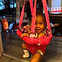 baby, child, pink_jumper, indoor, smiling, floor, household_items, bottle, orange_soda, legs, feet, bandages, face, toy, flooring, doorway, storage, clutter, socks, hanging