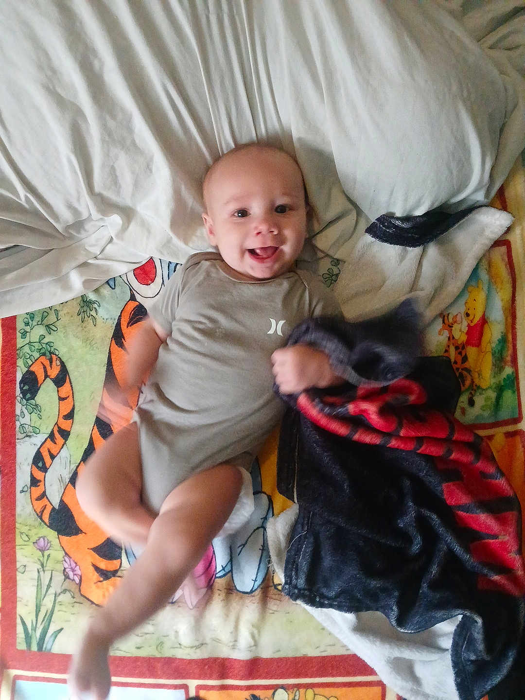 Erutan is registered to the contest to win money with this photo: baby, infant, smiling, blanket, cartoon, tiger, winnie_the_pooh, pillow, clothing, fabric, motion_blur, hand, foot, happy, child, lying_down, indoors, playful, cute, person