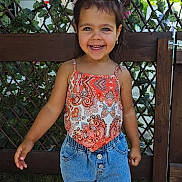 Irina Caruntu participe au concours pour gagner de l'argent avec cette photo : child, smiling, girl, outdoor, fence, ivy, hair_bows, summer, happy, denim_shorts, patterned_top, greenery, daylight, casual_clothing, portrait, cute, person, nature, sunlight, grass
