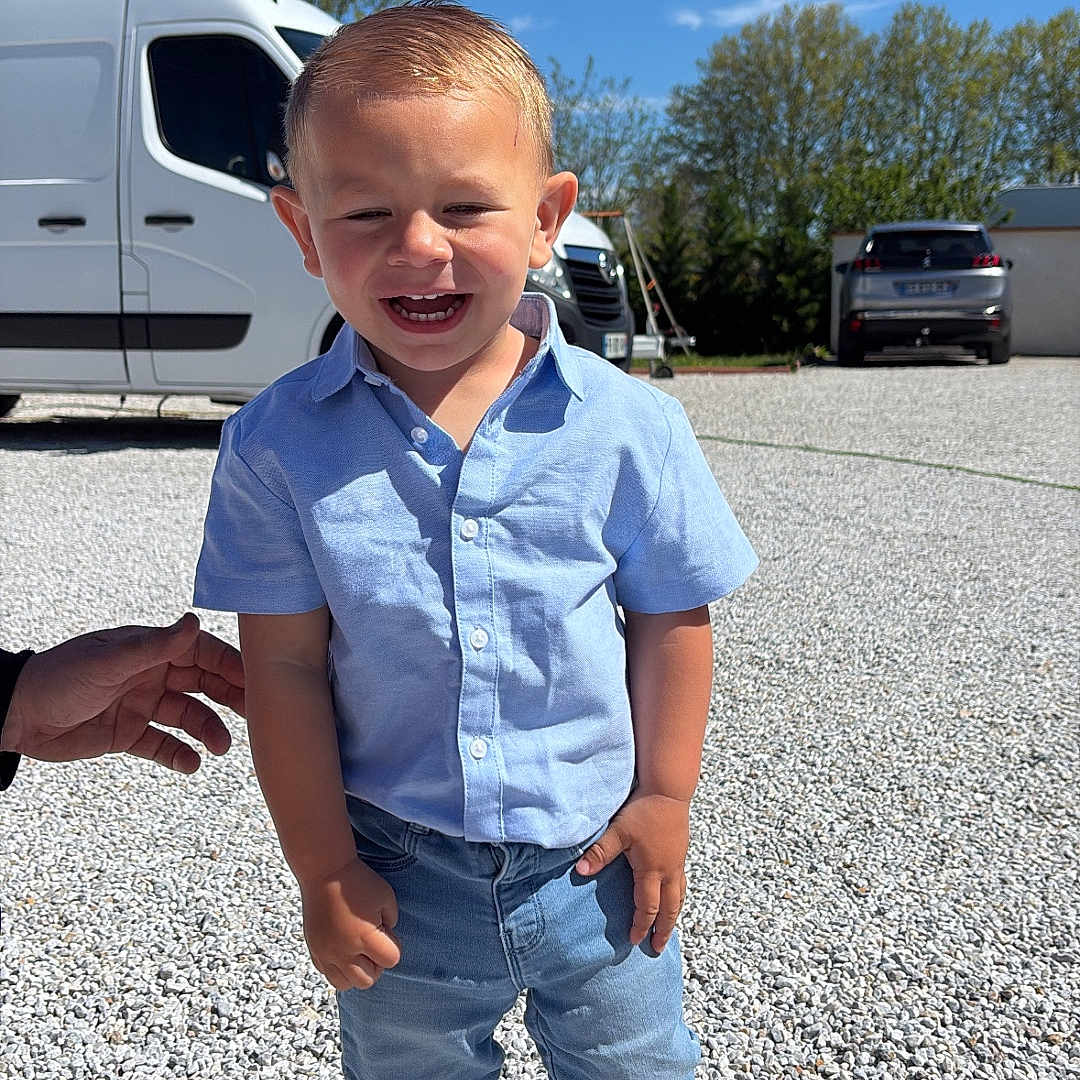 Zayden participe au concours pour gagner de l'argent avec cette photo : blue_crocs, blue_shirt, boy, car, casual_clothing, child, daylight, gravel, hand, happy, jeans, outdoor, portrait, sky, smiling, sunlight, toddler, trees, van, vehicle
