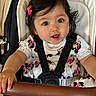 baby, child, stroller, seatbelt, dress, bow, black_hair, face, hand, safety_harness, infant, person, cute, smiling, indoor, clothing, grip, mickey_mouse, pink, happy