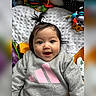 baby, child, infant, cute, smiling, happy, pony_tail, sweatshirt, grey_clothing, pink_logo, toys, playmat, soft_blanket, indoor, portrait, closeup, face, eyes, person, expression