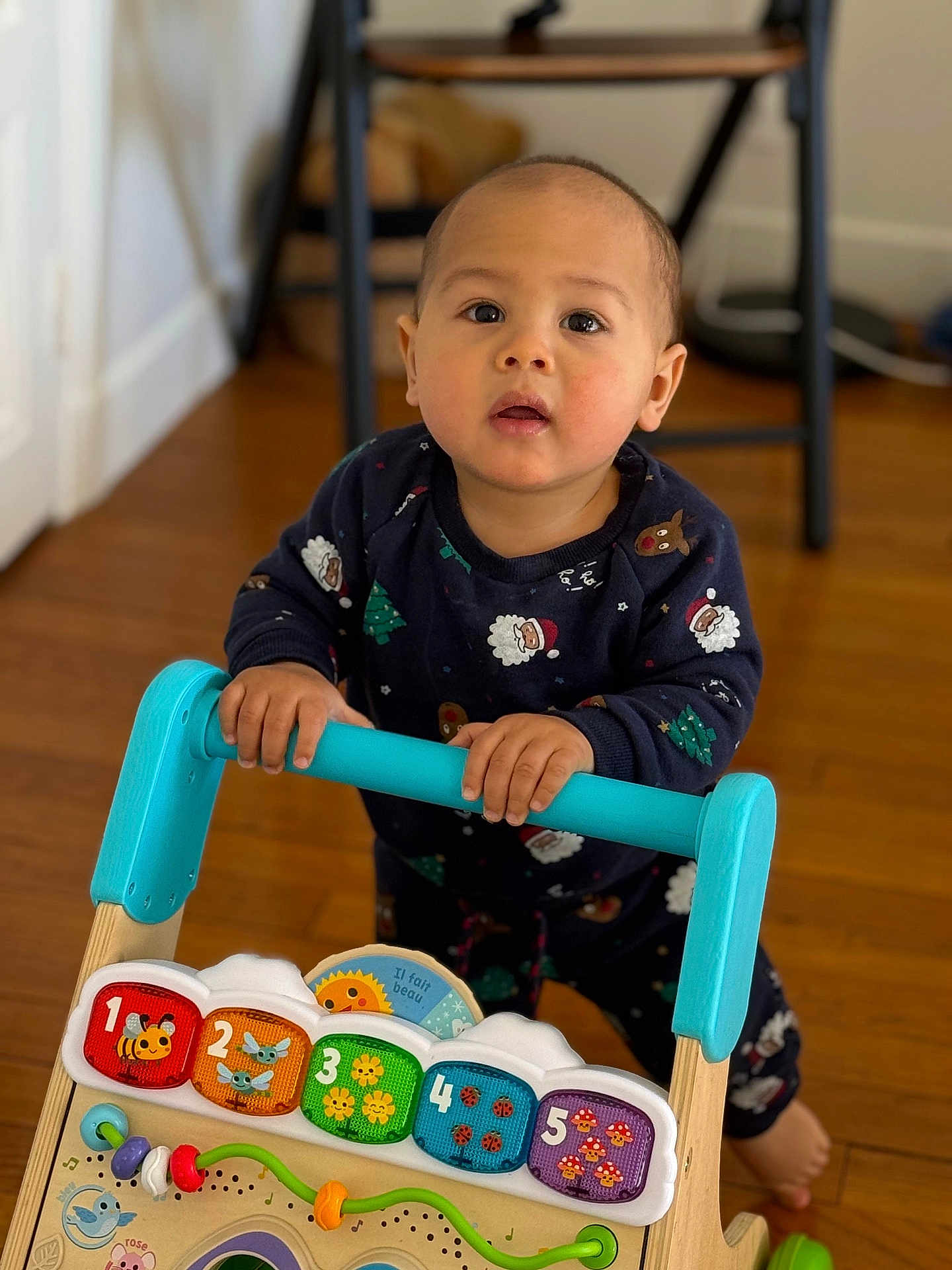 Asaël a rejoint le concours — aidez-le/la à gagner de superbes lots ! child, toddler, baby, toy, wooden_toy, walker, hands, hardwood_floor, pajamas, christmas_pattern, santa, reindeer, indoors, chair, face, eyes, curious, playing, bright_colors, smile