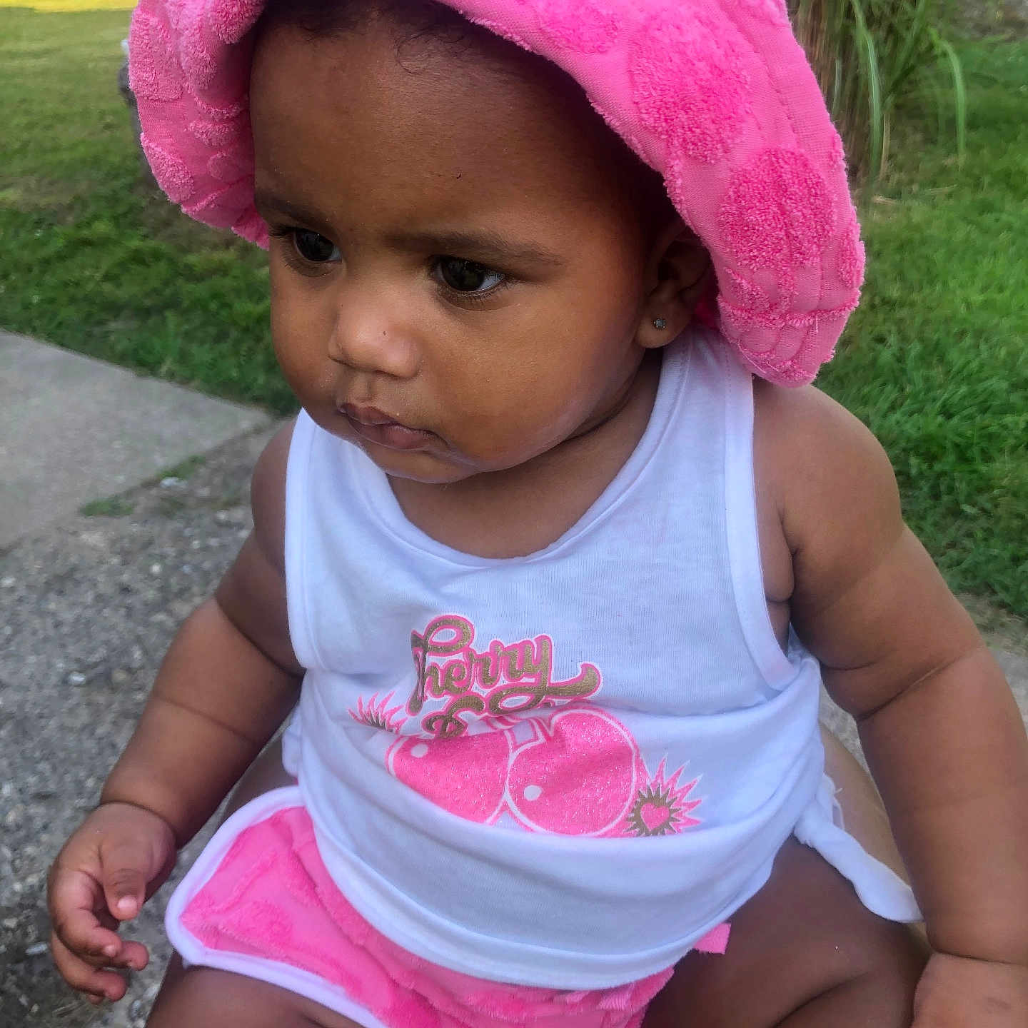 Scotlyn joined the competition — help win amazing prizes! baby, casual, child, cute, earrings, expression, grass, greenery, outdoor, person, pink_shorts, pink_towel, portrait, sidewalk, sitting, skin, summer, sunlight, toddler, white_tank_top