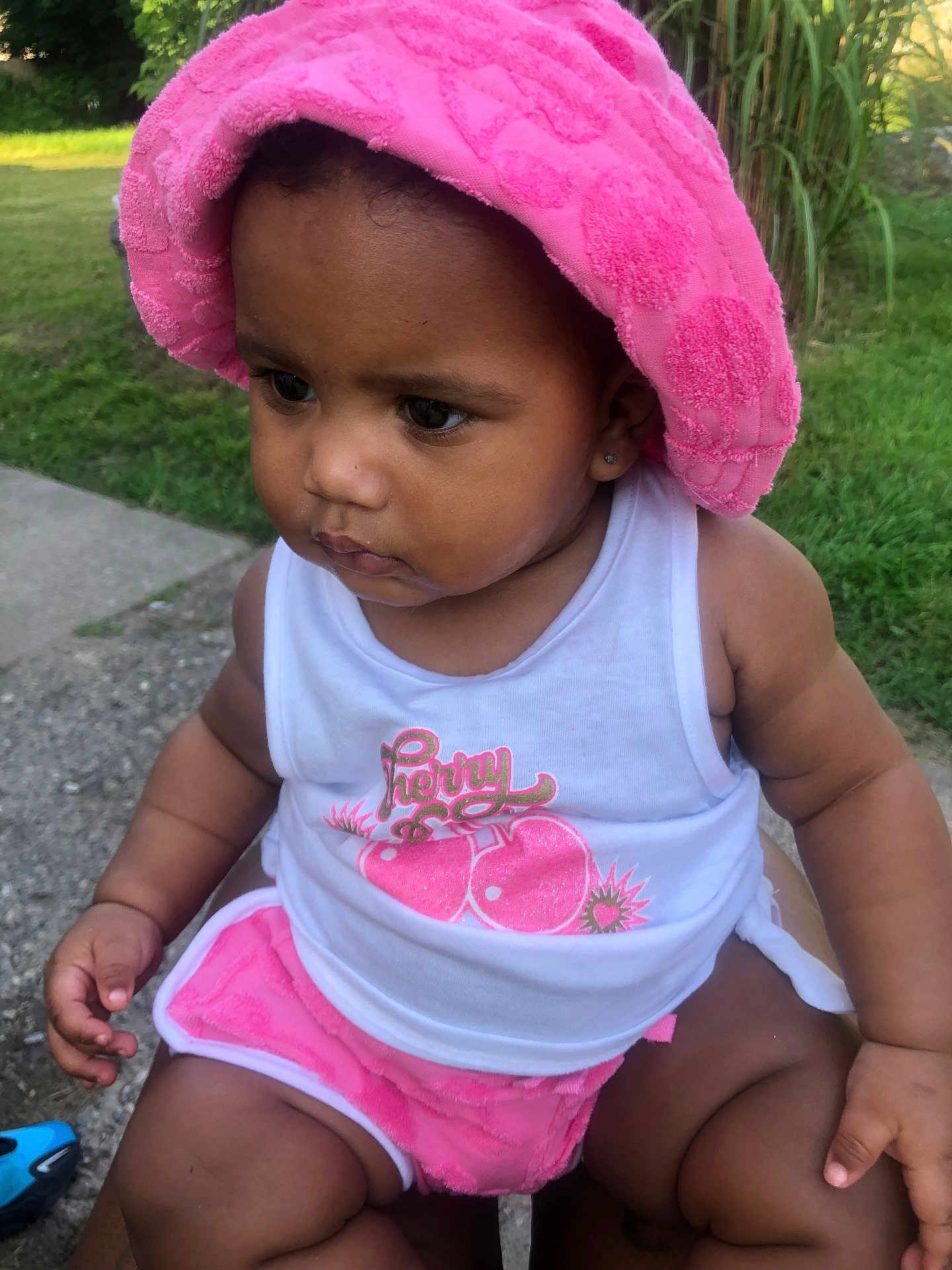 Scotlyn joined the competition — help win amazing prizes! toddler, child, pink_towel, pink_shorts, white_tank_top, outdoor, greenery, grass, sidewalk, sitting, person, baby, cute, summer, sunlight, casual, portrait, expression, skin, earrings