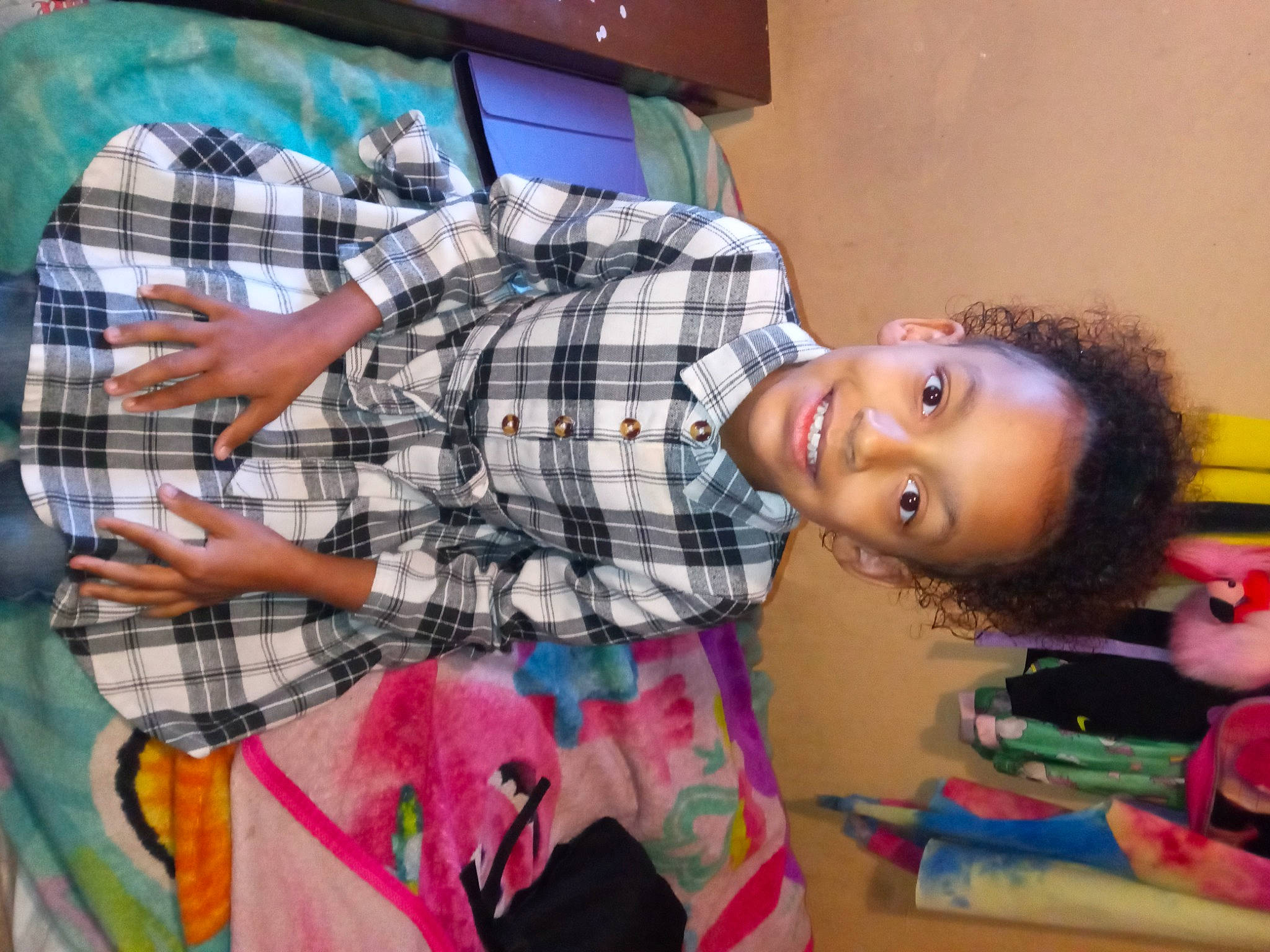 Love is registered to the contest to win money with this photo: child, comfort, facial_expression, fun, happy, joy, linens, pattern, person, plaid, room, sitting, smile, t_shirt, tartan