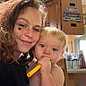woman, baby, indoor, smile, face, child, toy, holding, kitchen, cabinet, curly_hair, star_sticker, cheek, blond_hair, diaper, furniture, household_items, portrait, candid, warm_light