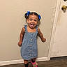 bear_slippers, blue_dress, braids, casual_clothing, child, door, full_body, girl, hair_bows, home, indoor, playful, portrait, slippers, smiling, standing, toddler, tongue_out, wall, wood_floor
