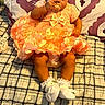 baby, child, dress, headband, pacifier, sitting, bed, pillow, pattern, flower, white_socks, cute, indoors, celebration, holiday, infant, smile, orange_dress, accessory, happy_easter