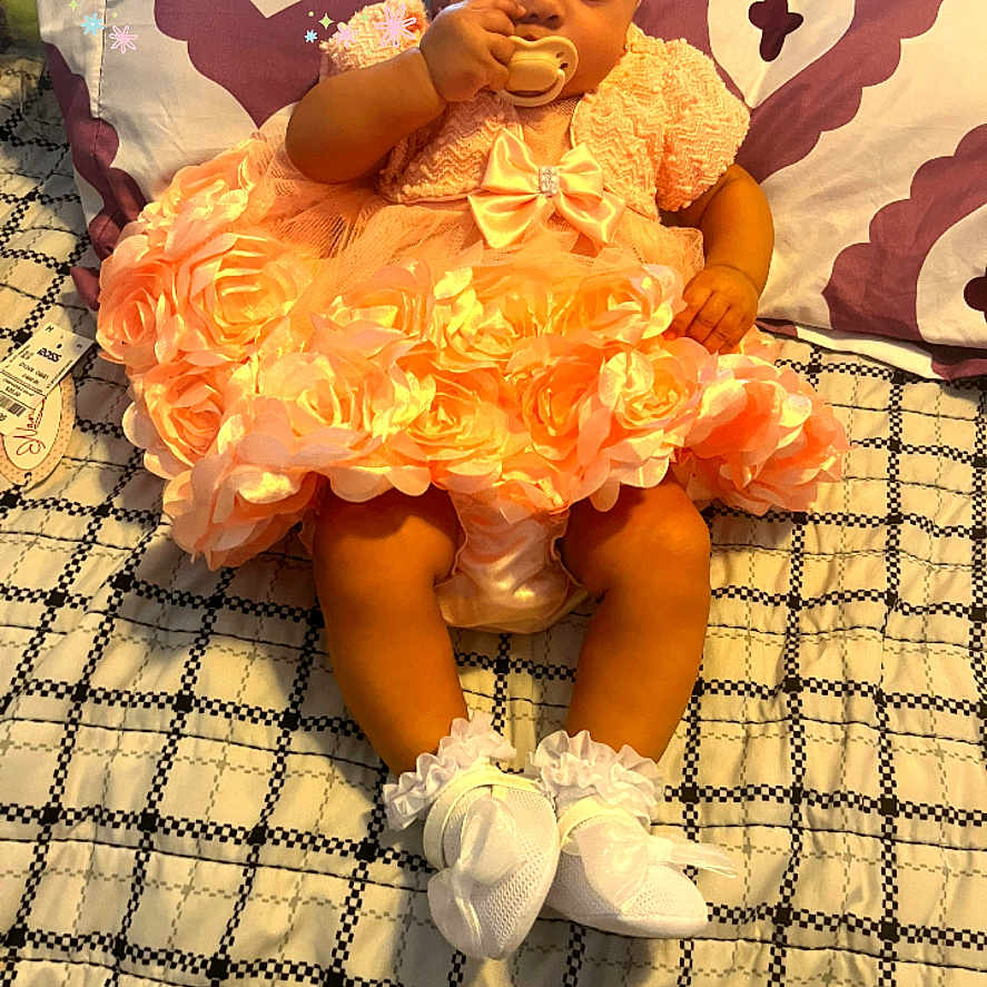 Amora is registered to the contest to win money with this photo: baby, child, dress, headband, pacifier, sitting, bed, pillow, pattern, flower, white_socks, cute, indoors, celebration, holiday, infant, smile, orange_dress, accessory, happy_easter
