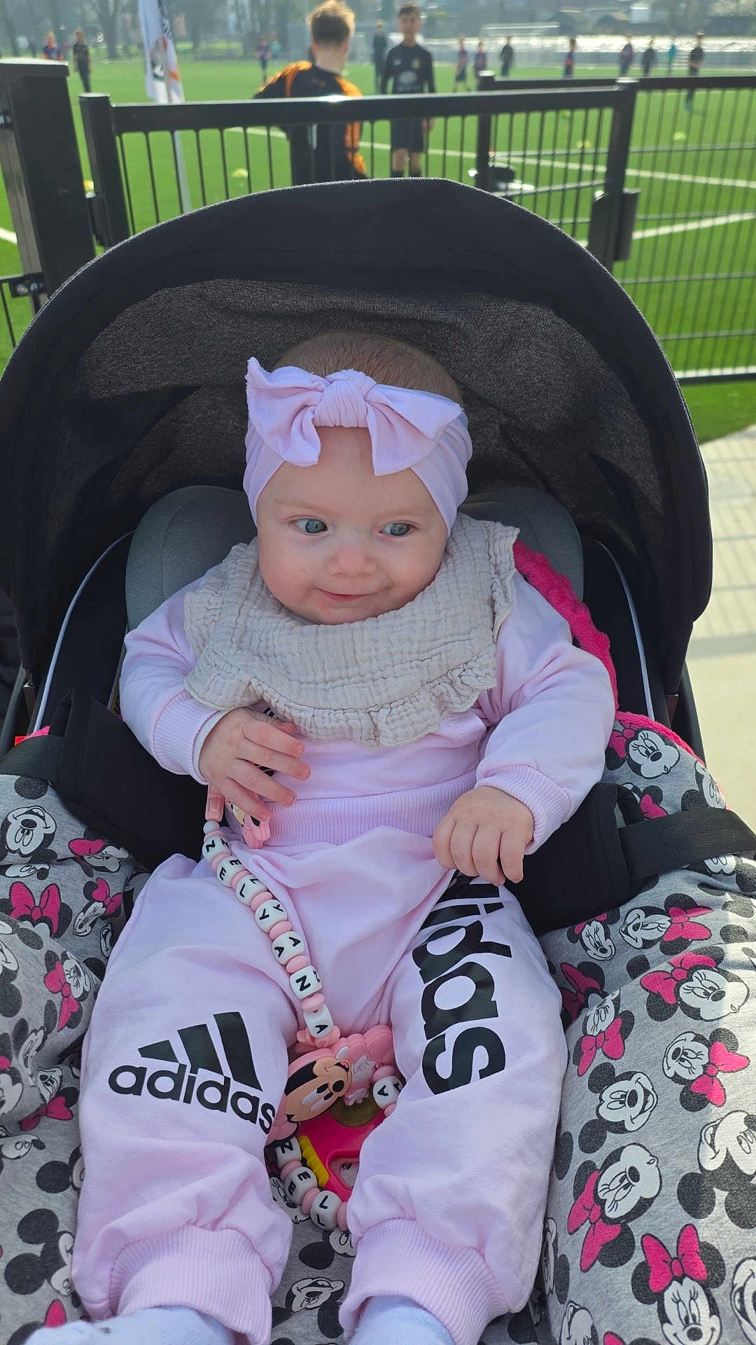 Zélyana a rejoint le concours — aidez-le/la à gagner de superbes lots ! baby, infant, stroller, headband, bow, bib, pink_clothing, adidas_logo, pacifier_clip, toy, car_seat, minnie_mouse_pattern, blanket, fence, soccer_field, soccer_players, outdoor, sunny, smile, portrait