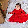 baby, red_dress, white_cushion, holiday_gifts, wrapped_presents, fluffy_texture, infant, portrait, indoor, christmas_theme, festive_clothing, cute, child, smiling, soft_lighting, cozy, warm_colors, holiday_decor, socks, young_child