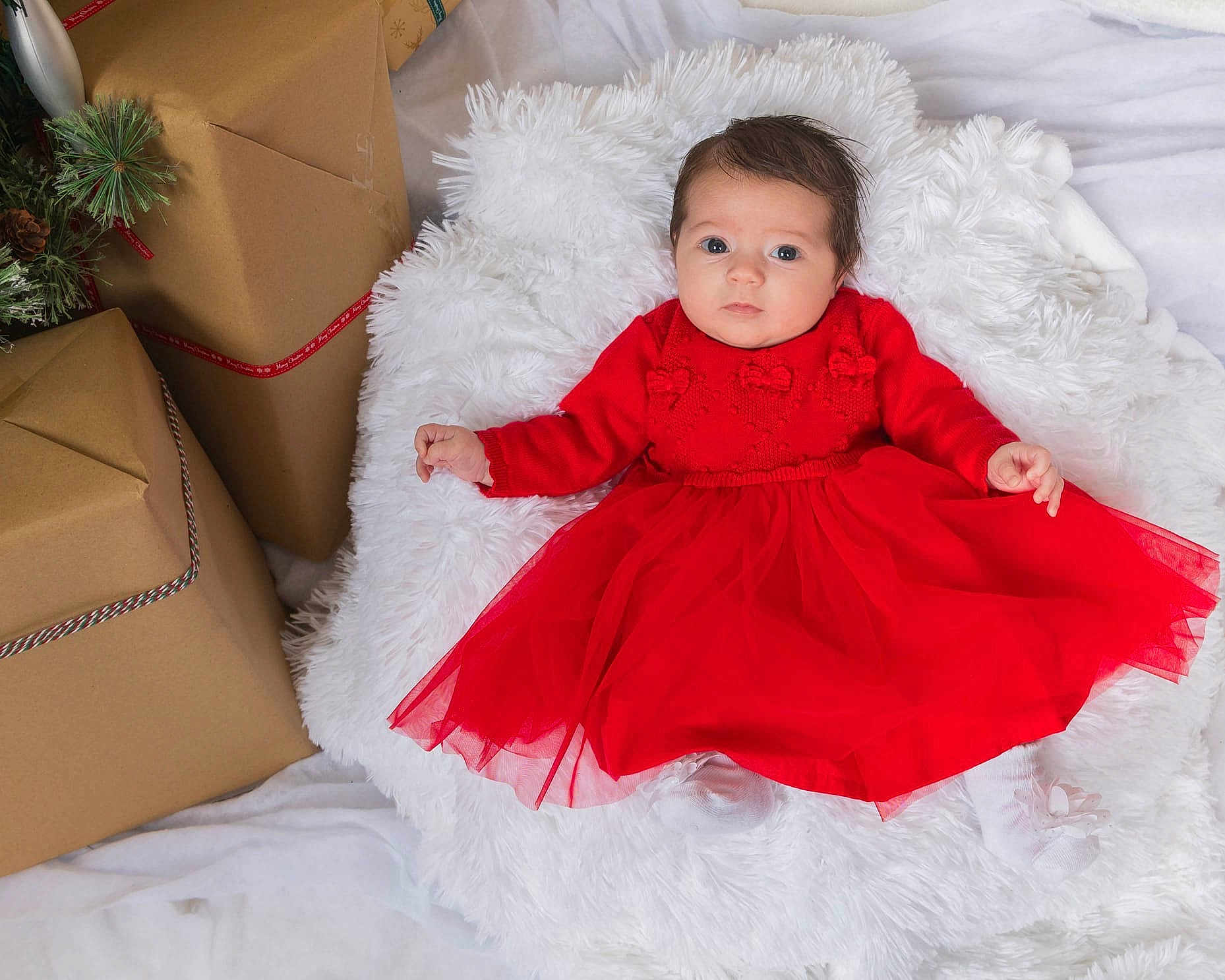 Amora Ocean is registered to the contest to win money with this photo: baby, red_dress, white_cushion, holiday_gifts, wrapped_presents, fluffy_texture, infant, portrait, indoor, christmas_theme, festive_clothing, cute, child, smiling, soft_lighting, cozy, warm_colors, holiday_decor, socks, young_child