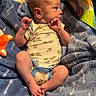 baby, infant, child, bouncer, blanket, portrait, sitting, lying_down, face, hands, feet, onesie, clothing, smiling, indoors, nursery, toy, colorful, cozy, home