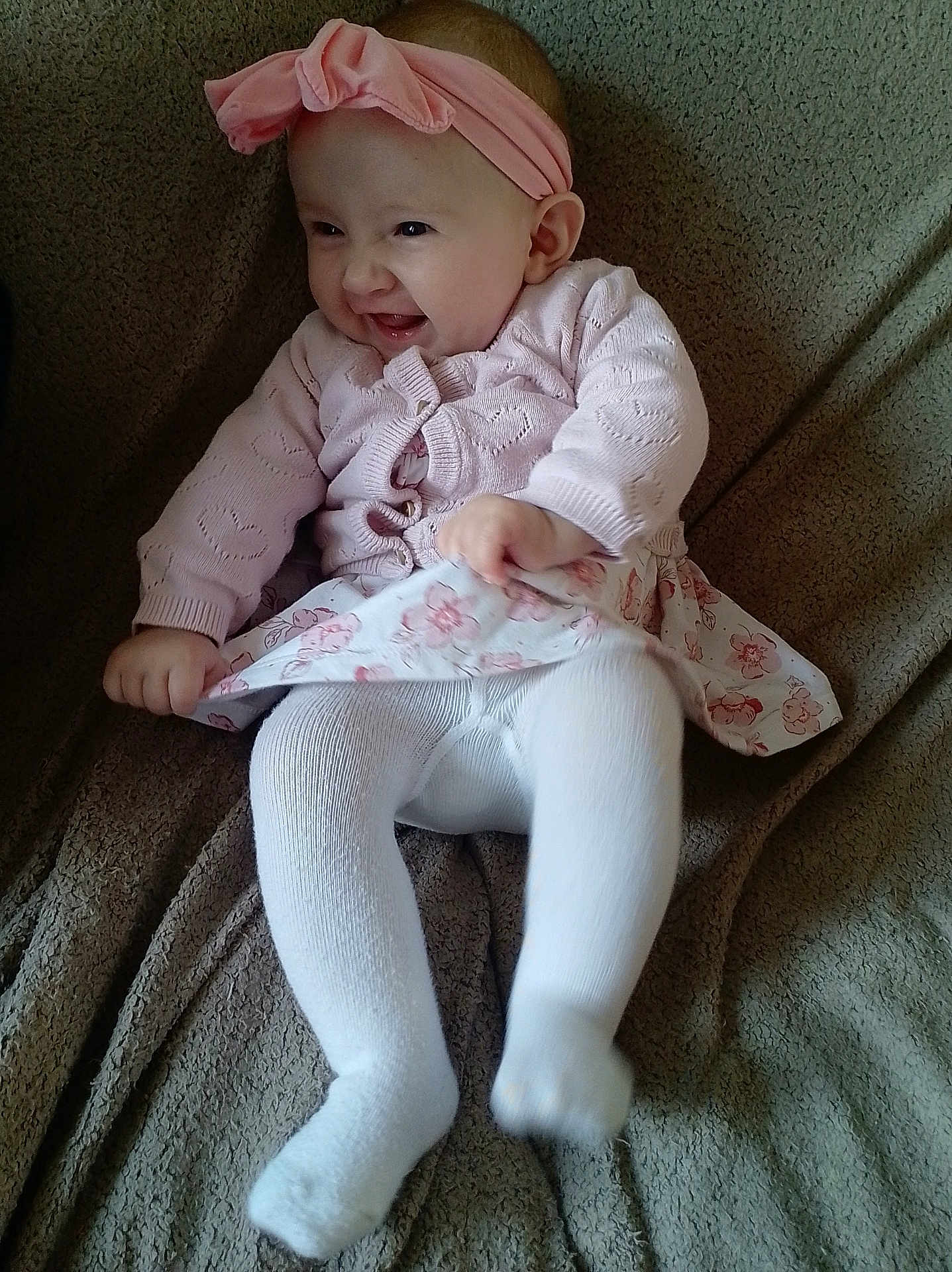 Ophélie a rejoint le concours — aidez-le/la à gagner de superbes lots ! baby, child, smile, pink_headband, sweater, floral_skirt, tights, sitting, blanket, happy, cute, indoor, infant, headband, person, clothing, portrait, toddler, joyful, cozy