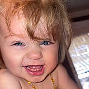 Maylynn is registered to the contest to win money with this photo: baby, toddler, child, smiling, laughing, close_up, face, blue_eyes, blonde_hair, messy_hair, teeth, necklace, amber_necklace, bare_shoulders, candid, portrait, indoor, window_blinds, joyful_expression, skin