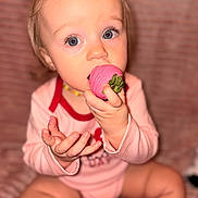 Maylynn joined the competition — help win amazing prizes! baby, toddler, child, face, blue_eyes, pink_strawberry, eating, food, onesie, sitting, hands, close_up, portrait, indoor, blanket, teething_necklace, long_eyelashes, cute, snack, holding
