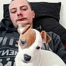 animal, brown_patch, casual, companion, couch, cute, dog, home, hoodie, indoor, looking_at_camera, man, pet, pillow, portrait, puppy, relaxed, sitting, white_dog, young_adult