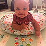 baby, infant, smiling, cushion, floral_pattern, floor_mat, indoor, child, cute, playful, person, toddler, happy, bright_eyes, short_sleeves, soft_lighting, home, toy_pattern, colorful, lying_down
