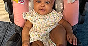 Romi joined the competition — help win amazing prizes! baby, child, infant, baby_seat, headband, pink_socks, floral_dress, toy, plush_toy, smiling, indoor, cushion, seat, happy, person, cute, face, hand, footwear, comfort
