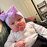 baby, pacifier, headband, purple_bow, onesie, floral_pattern, infant, close_up, person, indoor, shelf, door, hand, clothing, face, skin, cute, child, holding, room