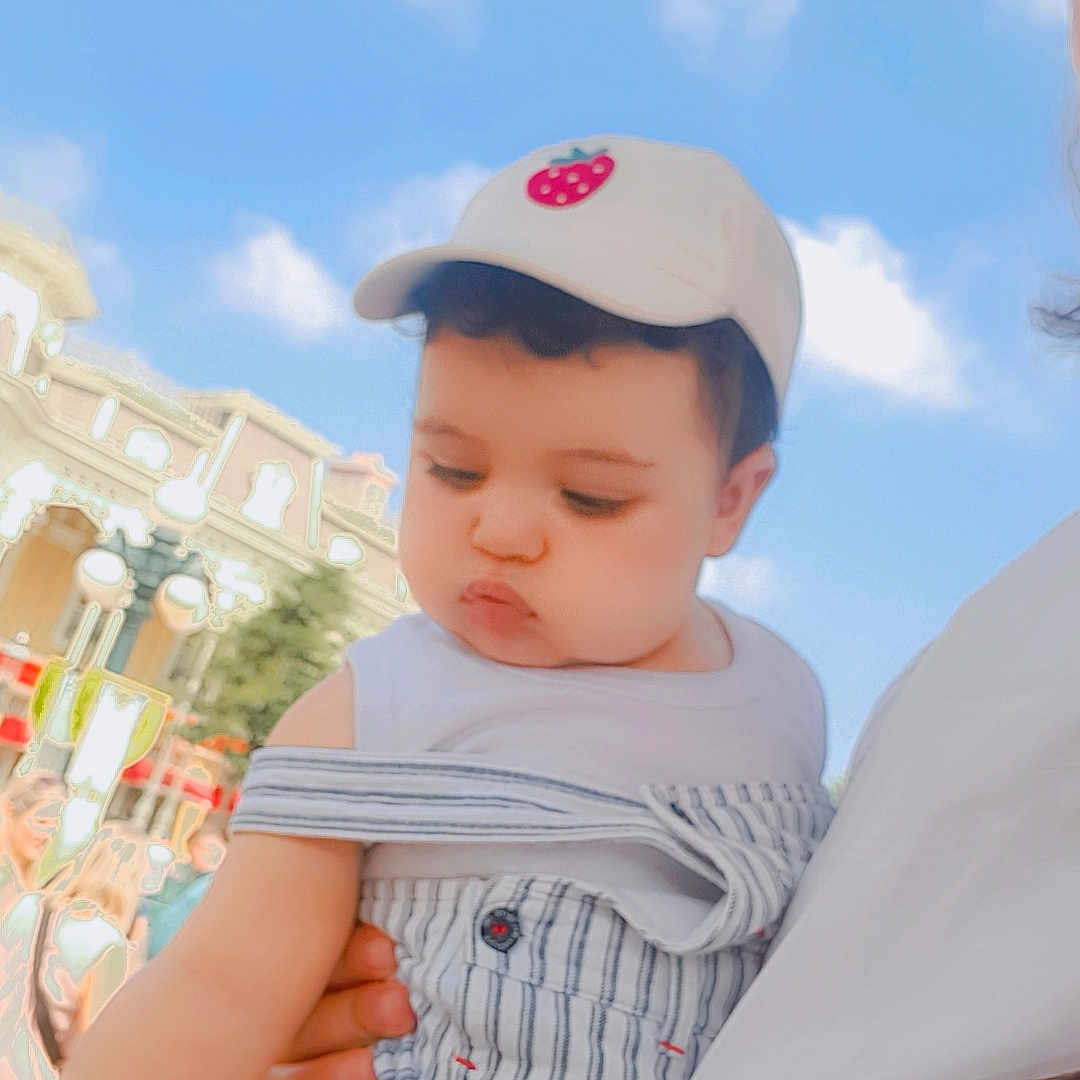 Yahya a rejoint le concours — aidez-le/la à gagner de superbes lots ! arm, baby, building, cap, casual_clothing, child, clouds, curious, cute, daylight, fashion, hat, holding, infant, outdoor, person, portrait, sky, striped_overalls, summer